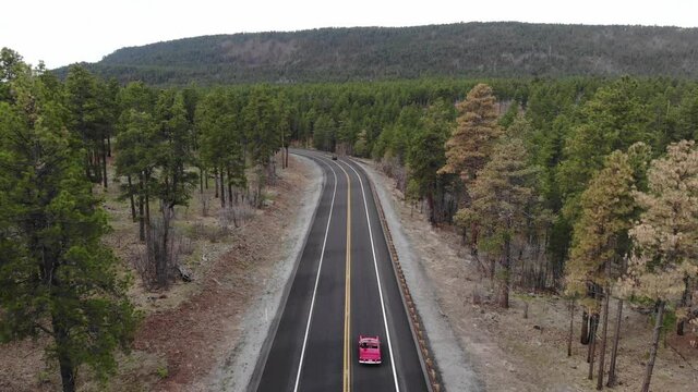 4k drone following red Ford Thunderbird in Arizona pine tree forest