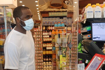 African American man standing in grocery store line wearing blue surgical face mask during Coronavirus pandemic