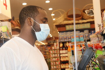Black Man checking out in grocery store wearing blue surgical face mask