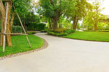 The gray curve pattern walkway, sand washed finishing on concrete paving, brown gravel on border, a smooth green grass lawn, trees with supporting and shrub in a garden