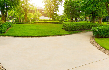 Gray curve pattern walkway, sand washed finishing on concrete paving, brown gravel on border, a smooth green grass lawn, trees with supporting and shrub in garden, good maintenance