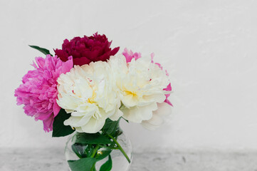 bouquet of fresh lush fragrant multi colored peonies in a stylish glass vase on a white background indoors