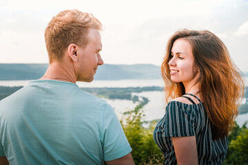 A man and a woman look at each other in love sitting on the edge of a mountain with a panorama of Russian nature with the Volga river and Islands