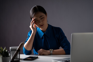 Asian woman in blue shirt was sick with headache working on a laptop at office.