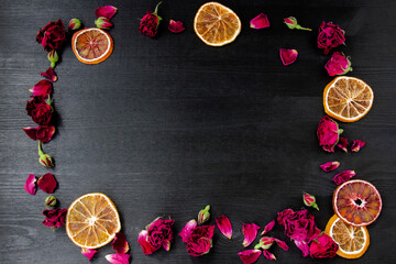 Wooden background with dry roses and petals and slices of dry orange with copy space. Flat lay composition with frame border made of dry roses and citrus.