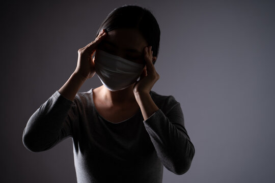 Asian woman wearing protective face mask was sick with headache touching her head and standing isolated on background.