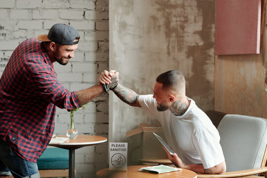 Hipster Young Male Friends Making Firm Handshake While Meeting In Hotel Lobby During Coronavirus Period