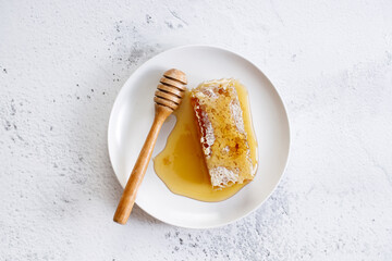 Honeycomb and honey dipper in white dish