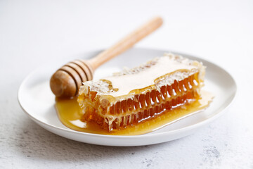 Honeycomb and honey dipper in white dish