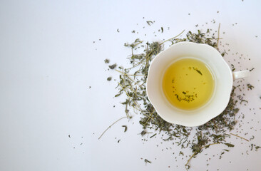 Tea with thyme in a white cup on a background of dried thyme. White background