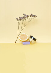 Cosmetic jar with yellow butter or cream, lemon and flower on yellow background. High quality photo