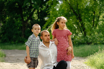 Obraz premium Amazing day. Happy family. Father and children look into the distance, against the background of green trees. Blurred backgroun