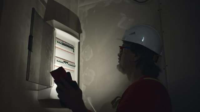 Electrician with flashlight switching fuses in fuse box