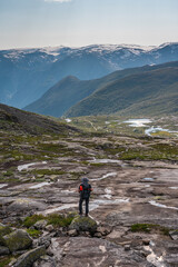 Young Asian man traveller with backpack trekking in Trolltunga mountain cliff, famous trekking route in Odda town, Norway, Scandinavia
