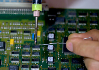 Male hands hold a soldering iron and solder against the background of an electronic Board with...