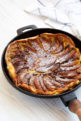Homemade Apple Dutch Pannekoek Pancake in a cast-iron pan on a white wooden background, low angle view.
