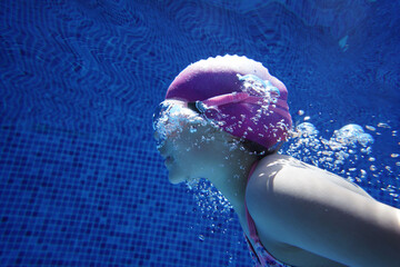 Young girl swimming underwater in blue pool