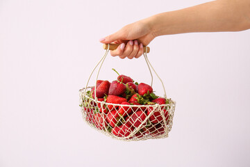 Female hand holding basket with fresh ripe strawberry on light background