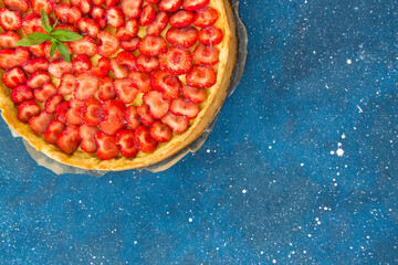 Fresh homemade strawberry shortcrust tart pie stuffed with custard vanilla cream . Sliced berries and mint leaf on the trendy phantom blue cosmos background. Free copy space. Top view.