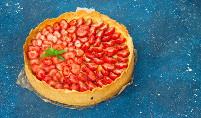 Fresh homemade strawberry shortcrust tart pie stuffed with custard vanilla cream . Sliced berries and mint leaf on the trendy phantom blue cosmos background. Free copy space. Top view.