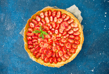 Fresh homemade strawberry shortcrust tart pie stuffed with custard vanilla cream . Sliced berries and mint leaf on the trendy phantom blue cosmos background. Free copy space. Top view.