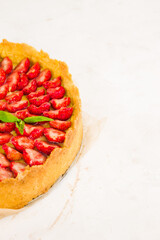 Fresh homemade strawberry shortcrust tart pie stuffed with custard vanilla cream . Sliced berries and mint leaf on the trendy white concrete background isolated. Free copy space. Top view.