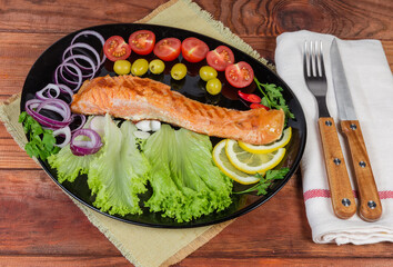 Serving of grilled trout fillet with vegetables on black dish