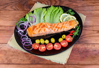 Portion of grilled trout fillet with vegetables on black dish