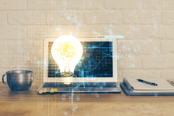 Computer on desktop in office with bulb icon hologram. Multi exposure. Concept of idea.