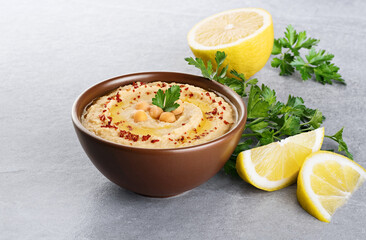 Chickpeas hummus with olive oil, paprika, parsley and lemon on a gray background.