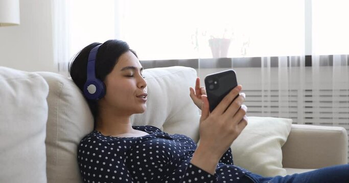 Asian young woman closed eyes resting on couch listen track through headphones play music on smartphone sing song feels carefree. Pastime and hobby, have fun at free time, leisure lazy weekend concept