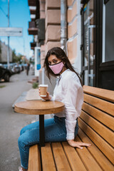 Woman in a medical mask drinks coffee on the street