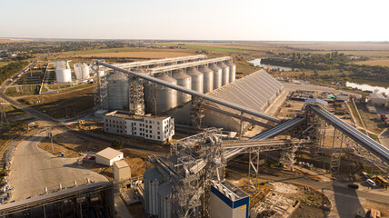 Aerial photo of big grain elevators near the sea. Modern grain terminal panorama. Metal tanks of elevator. Grain-drying complex construction. Commercial grain or seed silos at seaport. Steel storage