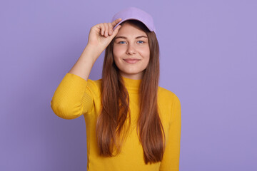 Naklejka premium Happy woman with pleasant appearance and long beautiful hair, looking at camera, keeping hand on visor of her baseball cap, expressive positive emotions, looks satisfied and confident.
