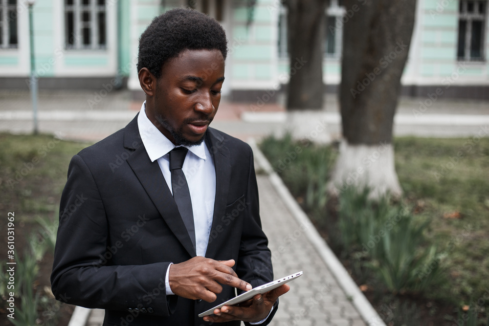 Wall mural African american handsome entrepreneur manages a bank using a tablet pc. Young adult multiethnic independence man building a career. Image with copy space.