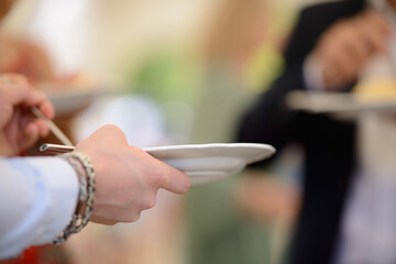 Obraz na płótnie Canvas Mani di un invitato che reggono piatto e forchetta in una cena in piedi all’aperto 