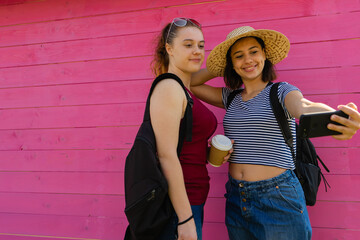 two young girls taking a selfie together on a pink background