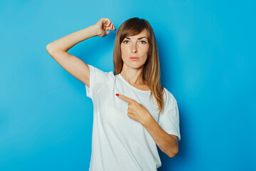 Young girl in a white T-shirt shows a finger on wet armpits from sweat on a blue background....