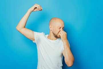 Young man in a white T-shirt with wet armpits from sweat on a blue background. Concept of excessive sweating, heat, deodorant