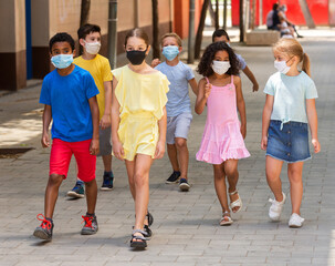 Obraz premium School children in protective medical masks walk along the street of a city