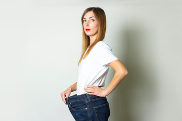 Young woman with a surprised face in oversize jeans on a light background. The concept of diet, a good result, weight loss, fitness