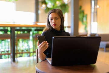 Young beautiful Asian businesswoman using phone and laptop at the coffee shop