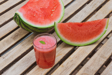 Summer watermelon juice with mint inside of a glass of water with slices of a half watermelon. Summer food and drinks concept.