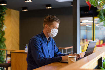 Young businessman with mask using laptop and sitting with distance inside the coffee shop