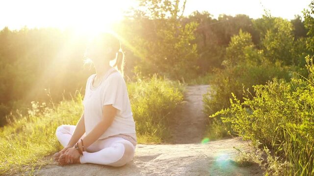 Fitness young woman is sitting Bound Angle Pose outside in park evening on background of bright sunray. Happy lady practicing yoga exercises in alone outdoors at green grass during sunset, slowmotion.