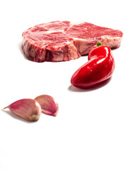 Rib eye steak in focus, red hot chilli pepper and two garlic cloves out of focus, premium cut of beef, Meat industry. White background.