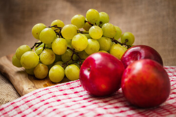 Still life, fresh juicy green grapes in focus, three nectarines in foreground out of focus on red and white kitchen towel, Hessian backdrop, Selective focus.