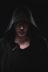 A low key portrait of a man in a hooded hand gesture makes a sperm hero mask. The concept of anonymity and privacy