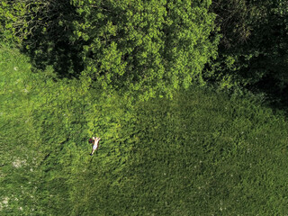 Aerial top down view on a man with naked torso laying on  a grass in a field by a trees, Summer season vibe concept.