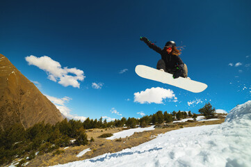 Stylish young girl snowboarder does the trick in jumping from a snow kicker against the blue sky...